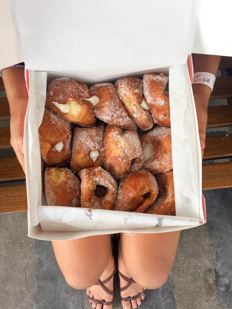 Open dozen box of mixed malasadas held in a lap