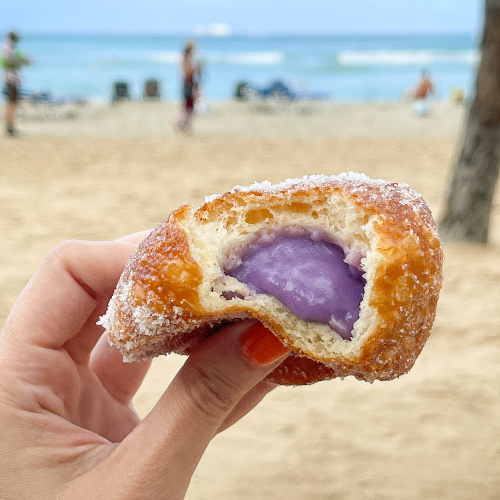 Hot malasada with ube filling held in front of the ocean