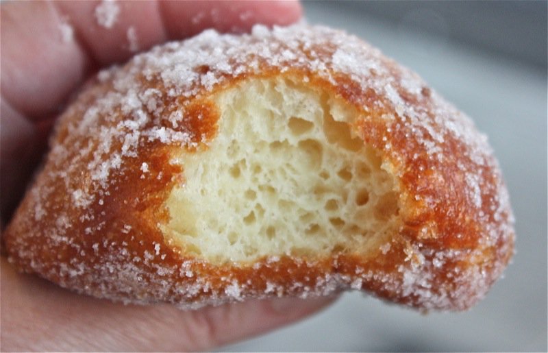 Close-up of a bitten hot malasada showing its light, fluffy interior